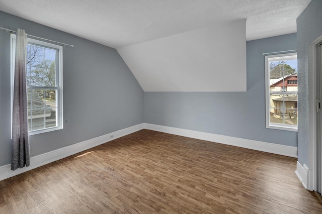 bonus room featuring wood finished floors, a textured ceiling, lofted ceiling, and baseboards