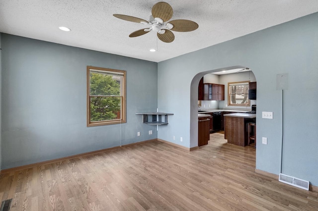 unfurnished living room with light wood finished floors, visible vents, a ceiling fan, arched walkways, and a textured ceiling