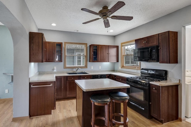 kitchen featuring a center island, a sink, black appliances, glass insert cabinets, and arched walkways