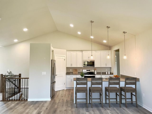 W255S5377 Primrose Ln, Waukesha, WI 53189 - kitchen featuring white cabinets, lofted ceiling, wood finished floors, a peninsula, and appliances with stainless steel finishes