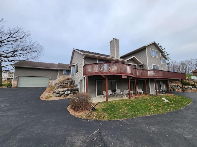 back of property featuring a chimney, a lawn, a deck, a garage, and aphalt driveway