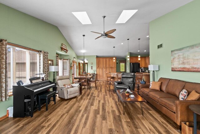 living room with high vaulted ceiling, a skylight, and wood finished floors