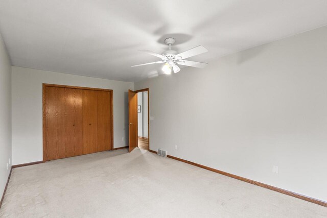 unfurnished bedroom featuring a ceiling fan, visible vents, baseboards, a closet, and light carpet