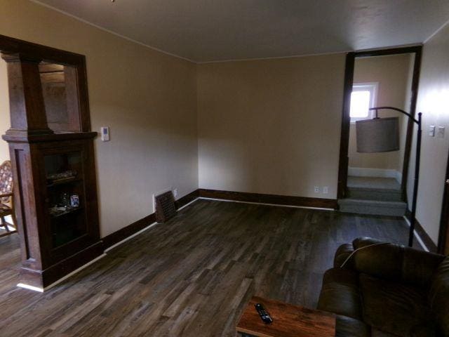 unfurnished living room with crown molding, baseboards, and dark wood-style flooring