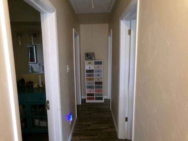corridor featuring attic access, baseboards, and dark wood-style floors