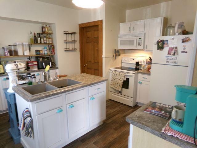 kitchen with dark wood-style floors, a sink, white appliances, a center island with sink, and white cabinetry