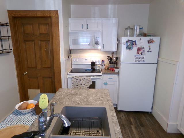 kitchen featuring a sink, white appliances, light countertops, white cabinets, and dark wood-type flooring