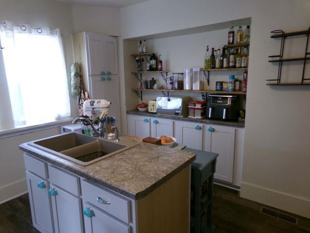 kitchen with dark wood-style flooring, an island with sink, a sink, and visible vents