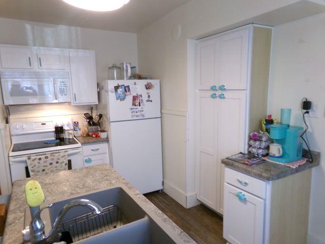 kitchen featuring white cabinets, wood finished floors, white appliances, and a sink