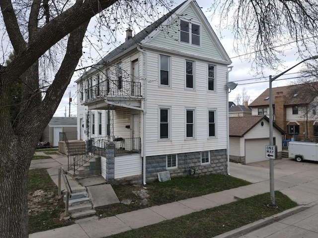 victorian-style house with an outbuilding, a balcony, a detached garage, and concrete driveway