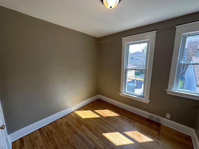 empty room featuring wood-type flooring, a healthy amount of sunlight, and baseboards
