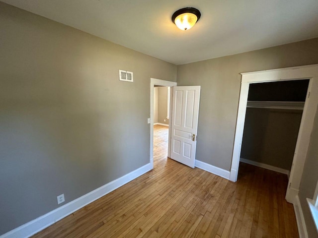 unfurnished bedroom featuring baseboards, hardwood / wood-style floors, visible vents, and a closet