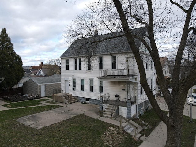 back of house with a chimney, a shingled roof, a balcony, a shed, and an outdoor structure