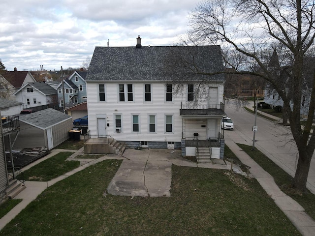 rear view of property with a lawn, roof with shingles, a balcony, and a patio