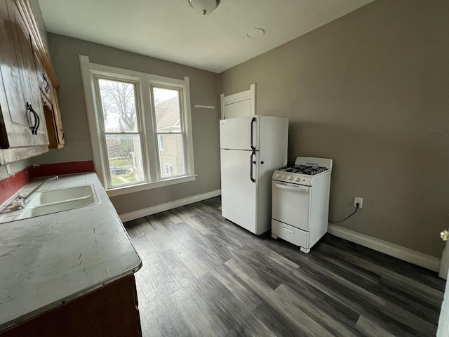 kitchen featuring dark wood-style floors, a sink, baseboards, white appliances, and light countertops