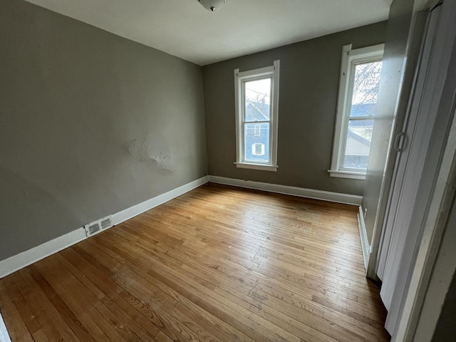 empty room with a wealth of natural light, hardwood / wood-style floors, visible vents, and baseboards