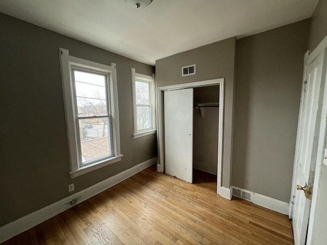 unfurnished bedroom featuring baseboards, a closet, visible vents, and light wood-style flooring