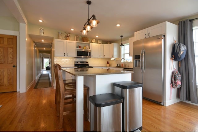 kitchen with a center island, white cabinets, light wood-type flooring, backsplash, and appliances with stainless steel finishes