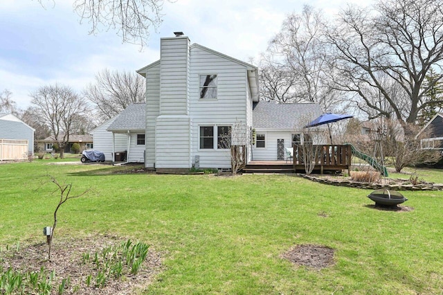 rear view of house with a fire pit, a chimney, a deck, a shingled roof, and a yard