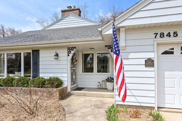 view of exterior entry with a shingled roof and a chimney