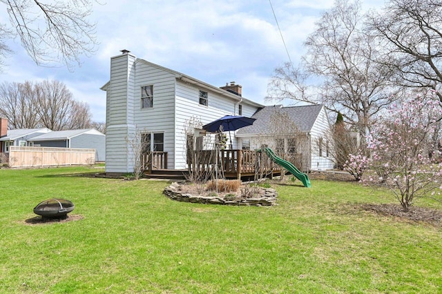 rear view of property with a fire pit, fence, a wooden deck, a chimney, and a lawn
