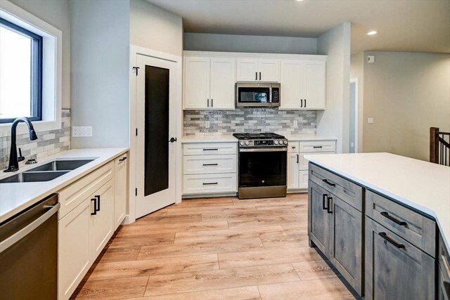 4021 Red Hawk Run, Black Earth, WI 53515 - kitchen featuring light wood finished floors, a sink, decorative backsplash, appliances with stainless steel finishes, and white cabinetry