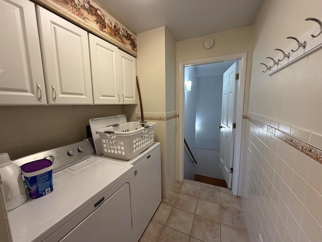laundry area featuring light tile patterned floors, cabinet space, washing machine and clothes dryer, tile walls, and a wainscoted wall