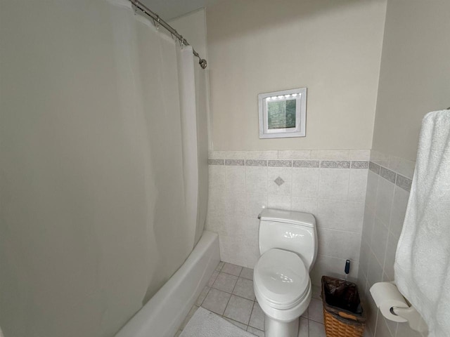 full bathroom with shower / tub combo with curtain, toilet, tile walls, tile patterned flooring, and wainscoting