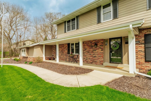 entrance to property featuring a yard, covered porch, and brick siding