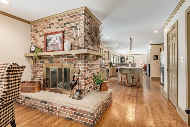living area with crown molding, light wood-style flooring, recessed lighting, and a brick fireplace