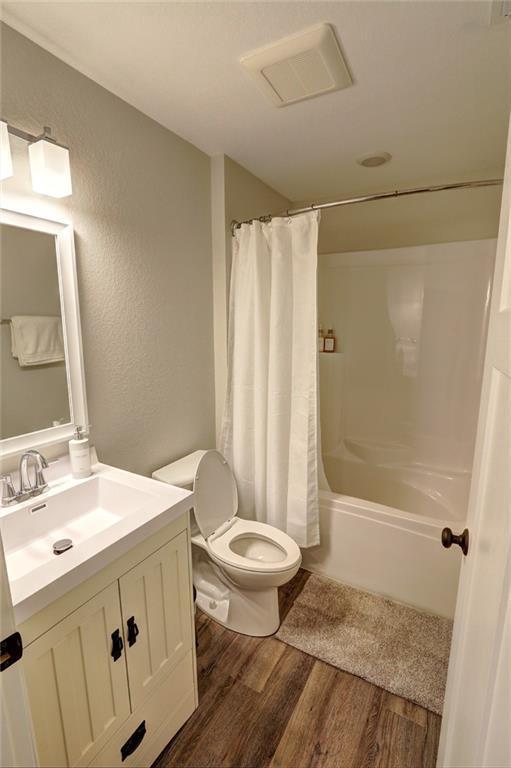 10230 Olker Rd, Hayward, WI 54843 - bathroom featuring shower / bathtub combination with curtain, wood finished floors, a textured wall, toilet, and vanity