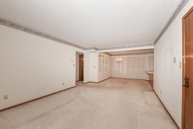 empty room featuring baseboards, a notable chandelier, and light carpet