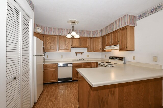 kitchen featuring white appliances, light countertops, a peninsula, under cabinet range hood, and dark wood-type flooring