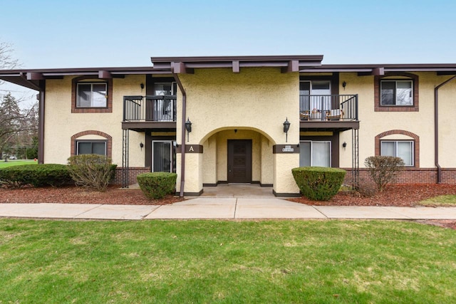 view of front of home with stucco siding, a balcony, and a front yard