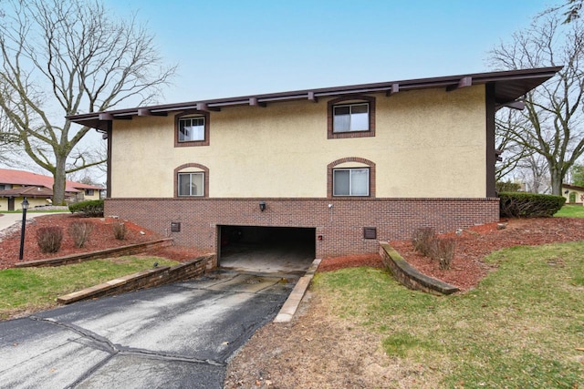 view of home's exterior featuring stucco siding, an attached garage, aphalt driveway, and brick siding