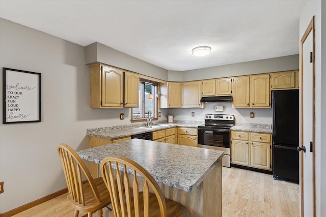 kitchen with black appliances, light wood-style floors, a breakfast bar area, light countertops, and under cabinet range hood