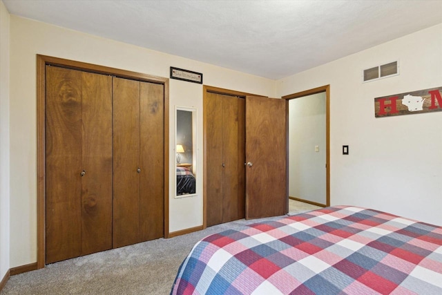 bedroom with two closets, visible vents, baseboards, and light carpet