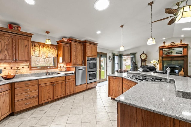 kitchen featuring brown cabinets, stainless steel appliances, a ceiling fan, light tile patterned floors, and a sink