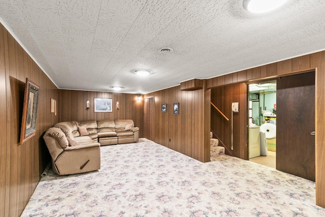carpeted living room with washer / dryer, wooden walls, and stairway