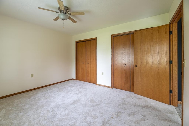 unfurnished bedroom featuring baseboards, carpet flooring, multiple closets, and ceiling fan