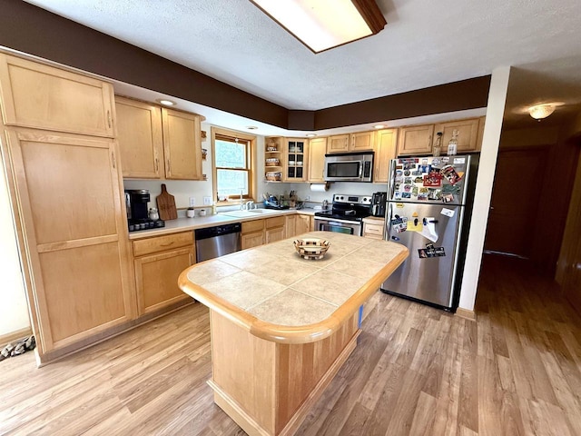 kitchen with light brown cabinets, a center island, tile countertops, light wood-style flooring, and appliances with stainless steel finishes