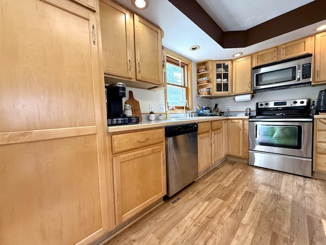 kitchen with light brown cabinetry, light wood-style floors, open shelves, light countertops, and appliances with stainless steel finishes