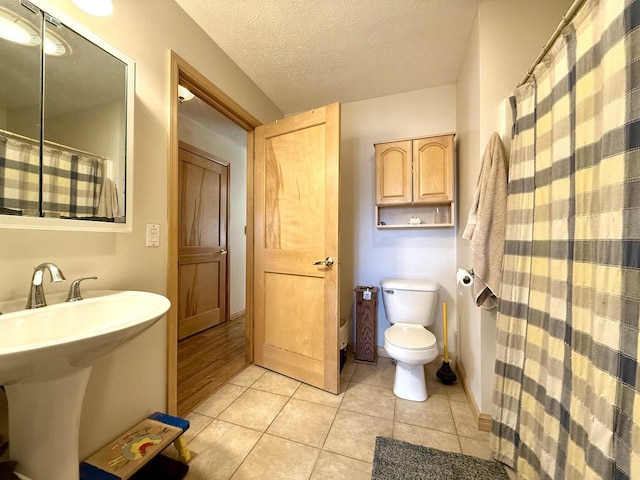 full bath featuring a sink, a textured ceiling, a shower with curtain, toilet, and tile patterned flooring