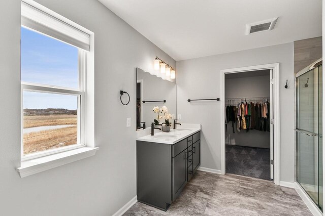 full bath with a sink, double vanity, a stall shower, visible vents, and a walk in closet