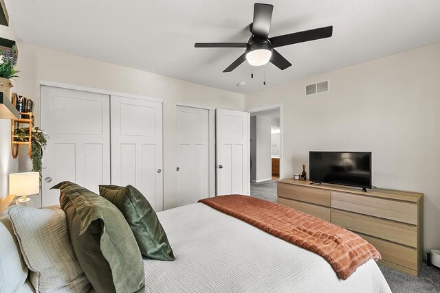 bedroom featuring two closets, visible vents, carpet flooring, and ceiling fan