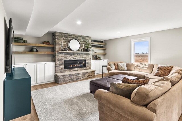 living room with light wood finished floors, a stone fireplace, and recessed lighting