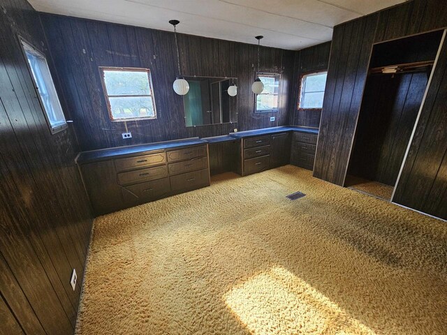 kitchen with built in desk, wooden walls, visible vents, light carpet, and hanging light fixtures