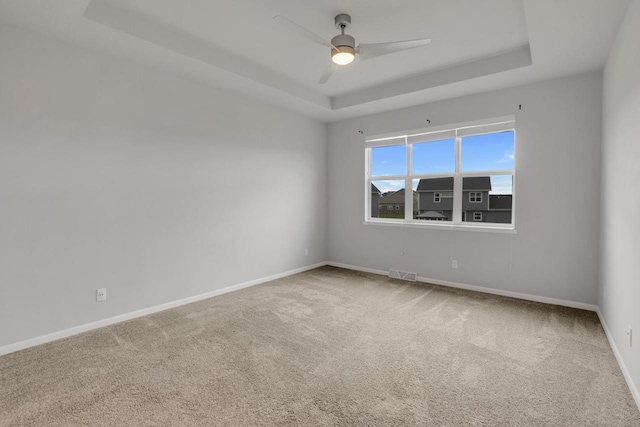carpeted spare room with baseboards, a ceiling fan, a tray ceiling, and visible vents
