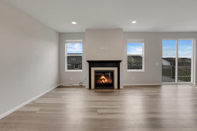 unfurnished living room featuring light wood finished floors, a glass covered fireplace, visible vents, and recessed lighting