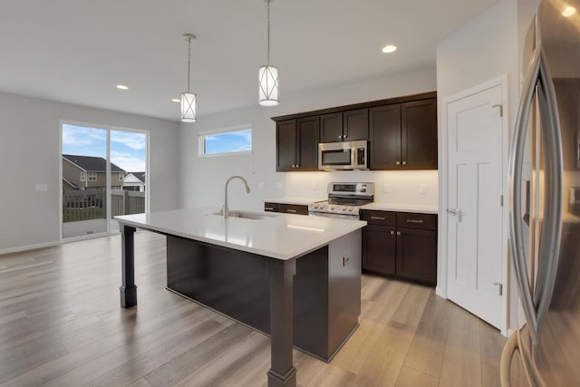kitchen with a sink, dark brown cabinetry, light wood-style floors, light countertops, and appliances with stainless steel finishes